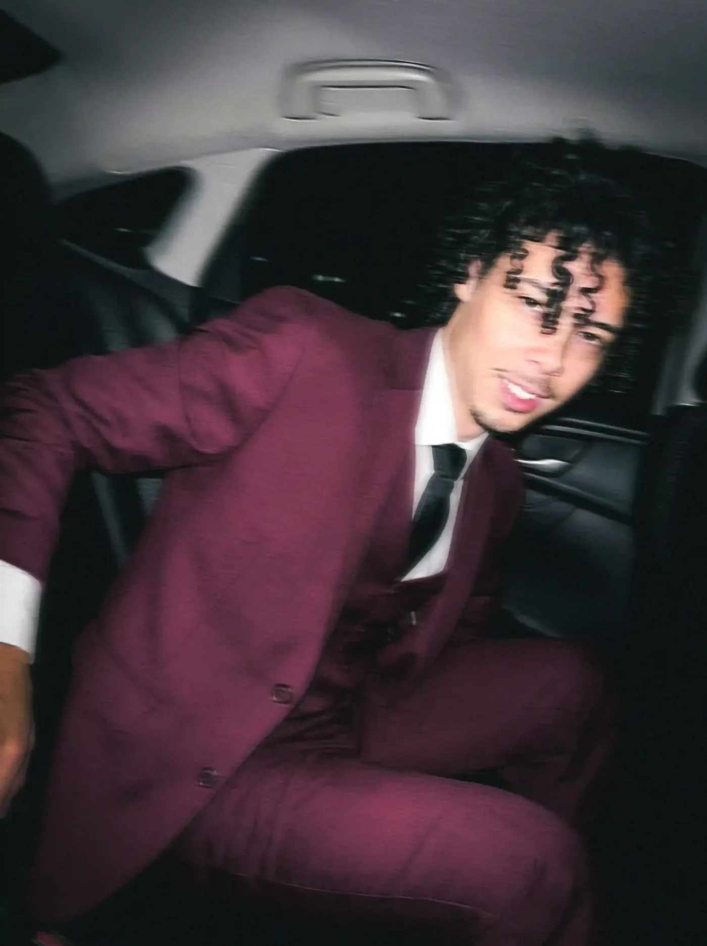 Bryan Haller em foto com efeito de movimento, estilo paparazzi, vestindo terno vinho