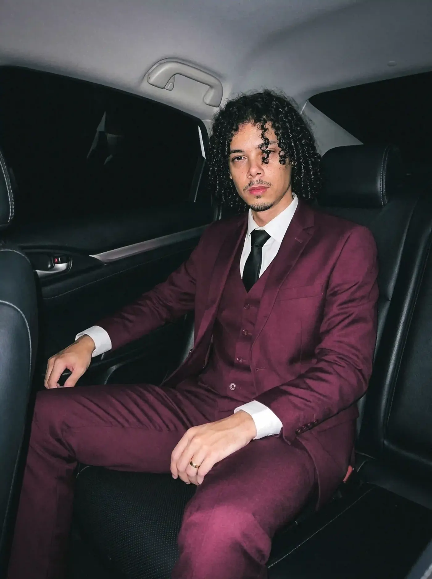 Bryan Haller de terno vinho no banco traseiro de um carro, na virada de 2026
